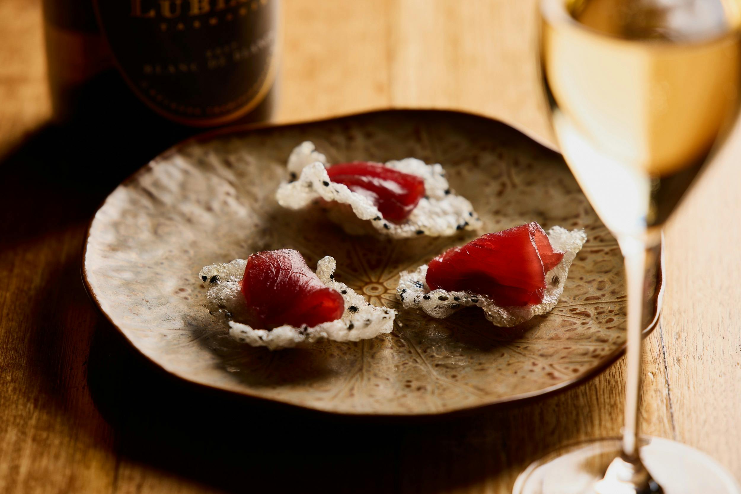 A restaurant canape dish, feautring freshly sliced bluefin tuns on a cracker, with a glass of wine.