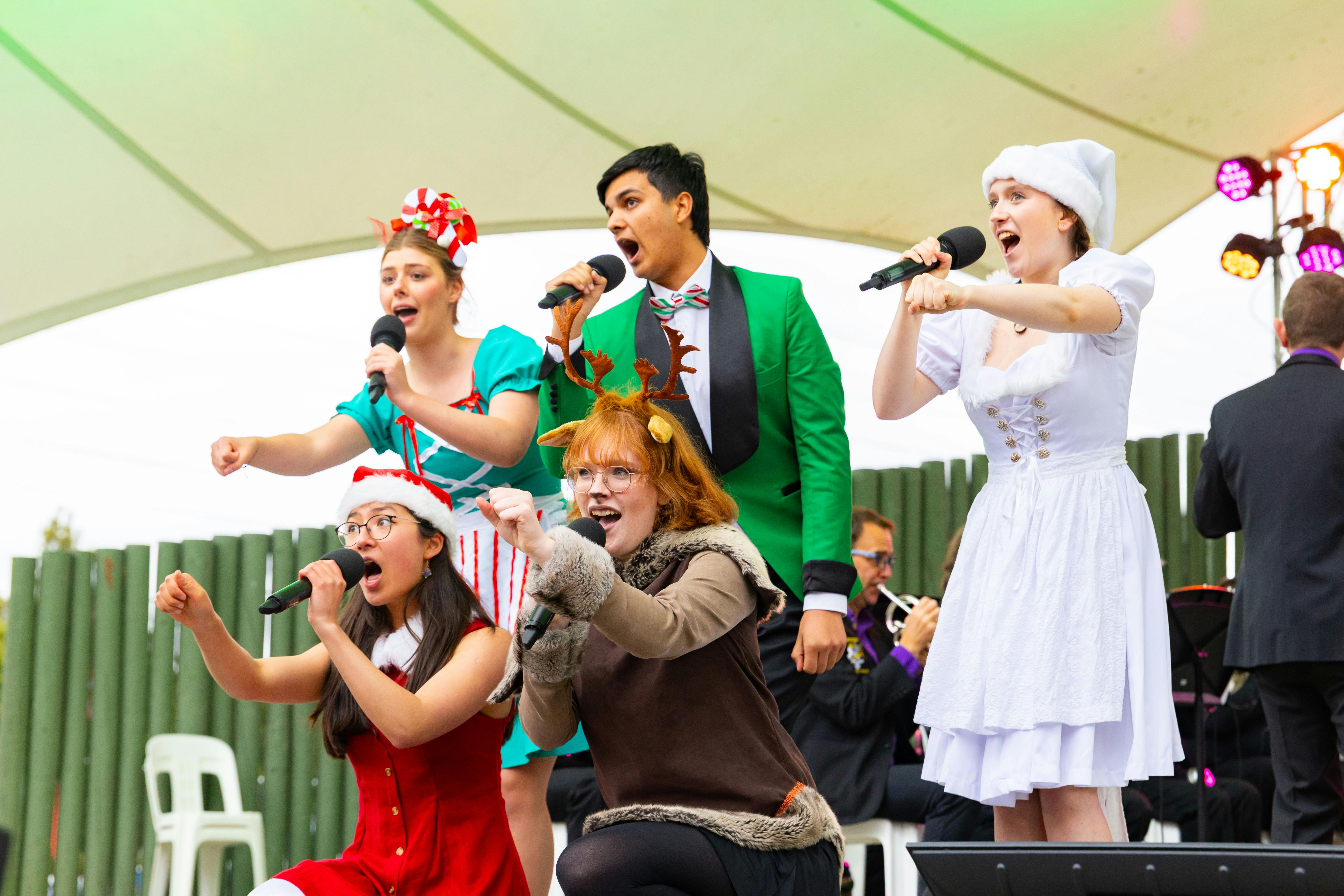 Costumed singers in reindeer antlers and santa suits singing Christmas Carols on stage