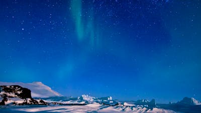 Aurora Australis glows in the night sky above a snowy, mountainous landscape.