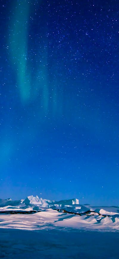 Aurora Australis glows in the night sky above a snowy, mountainous landscape.