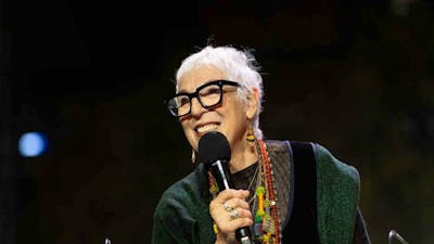 A woman with short grey hair and glasses holding a microphone on stage