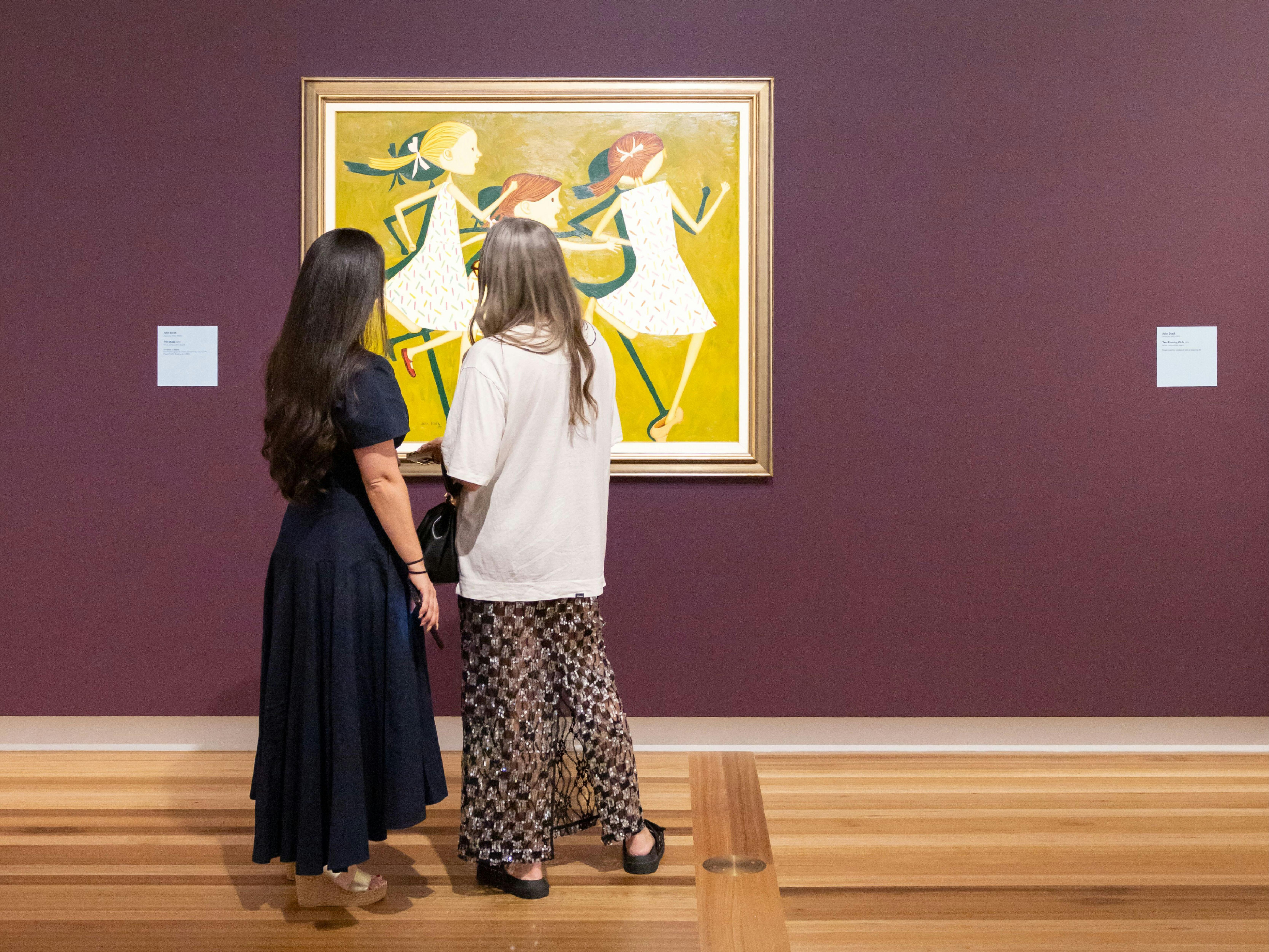 Two people in formal clothing view a portrait hung on a Gallery wall depicting three young girls.