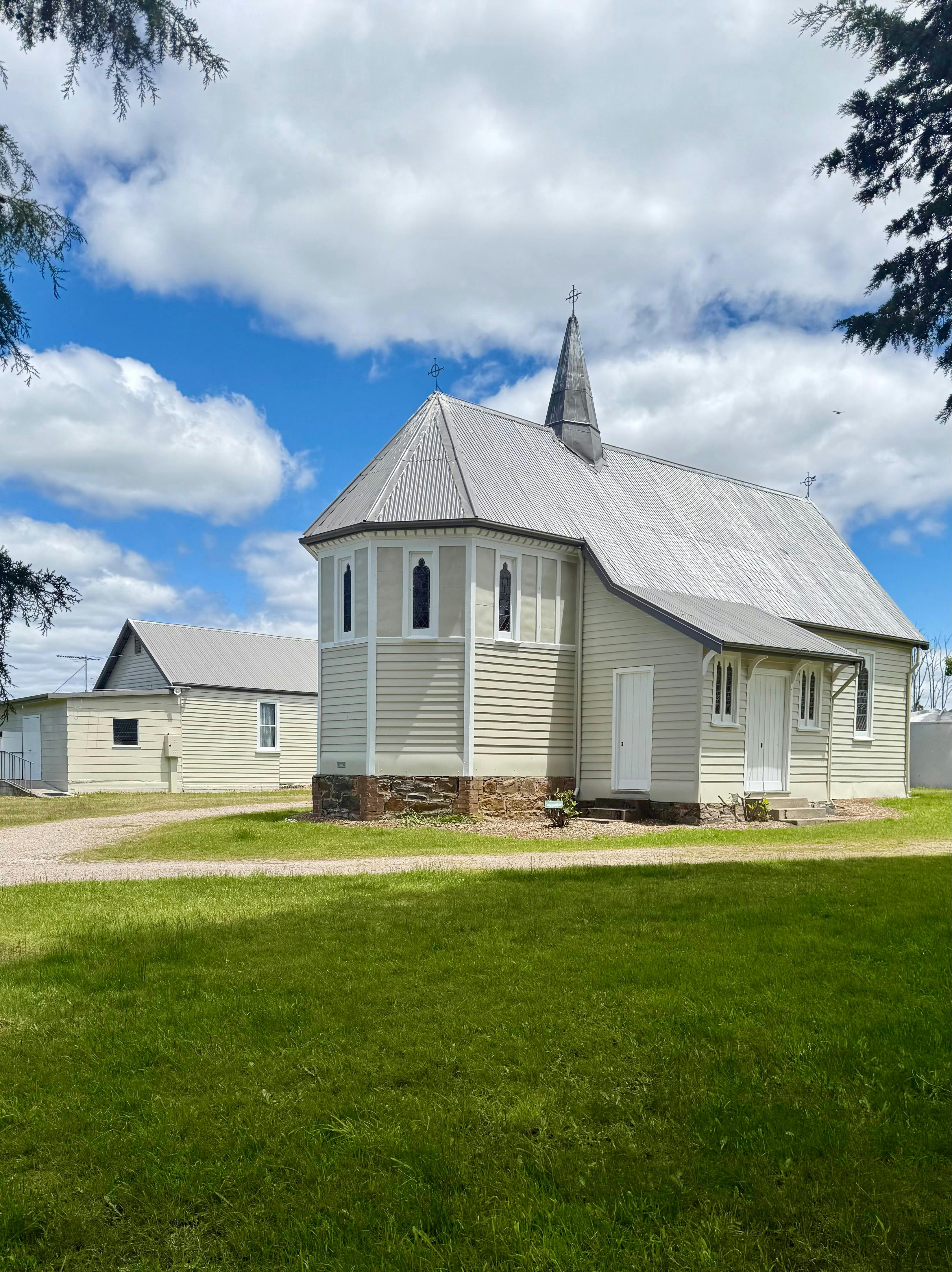 Country church in foreground with hall behind framed by trees