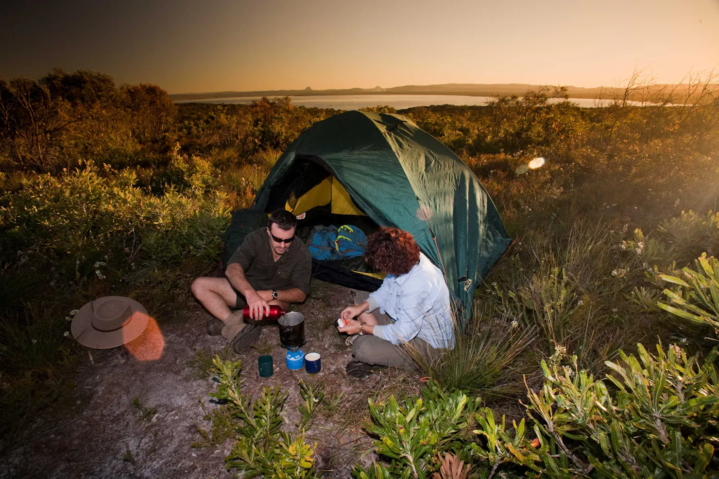 Two people sitting outside their pitched tent with a lake in the background.