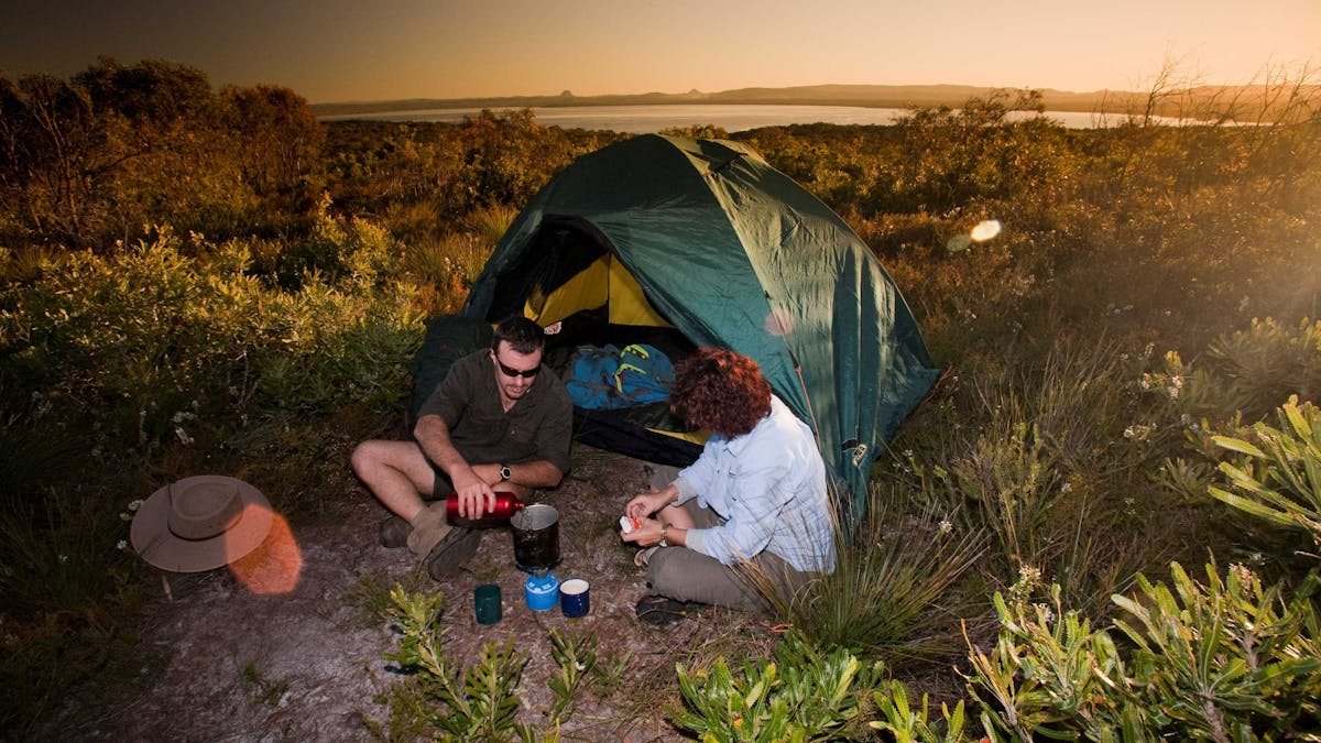 Two people sitting outside their pitched tent with a lake in the background.