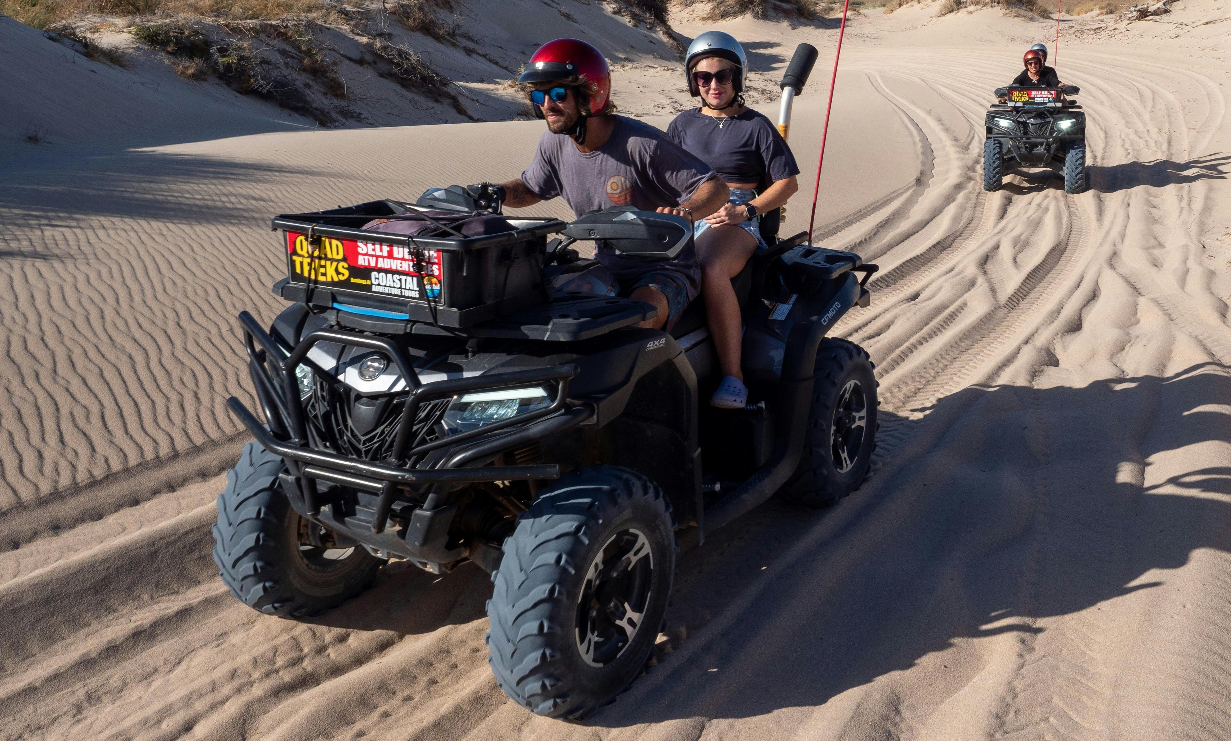Couple driving quad bike on sandy track. Second quad bike on sandy track in the background