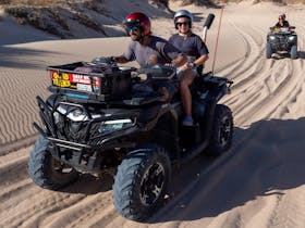 Couple driving quad bike on sandy track. Second quad bike on sandy track in the background