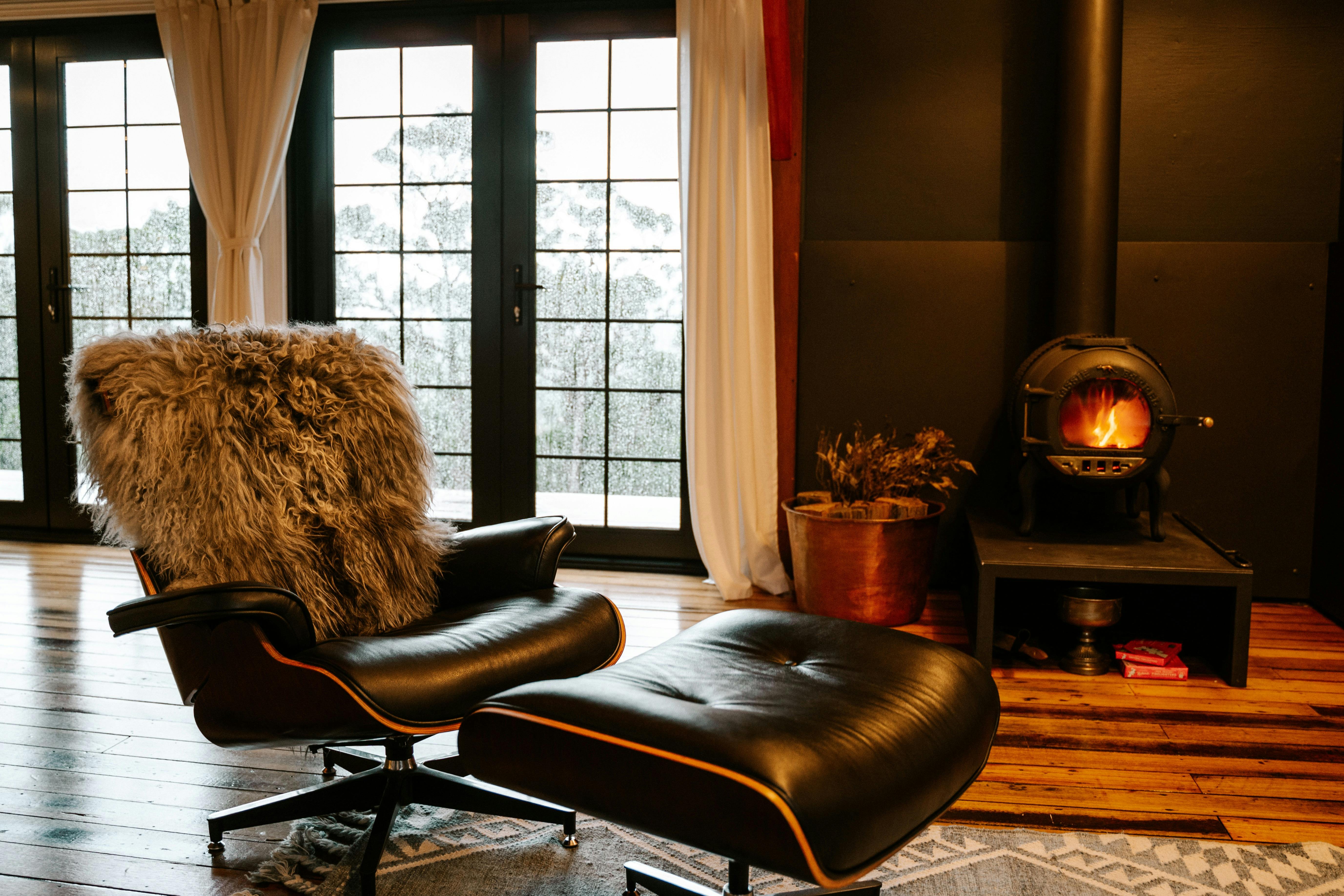 A leather armchair, covered in a sheepskin rug with a wood fire burning, rain outside