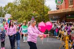 A woman in a pink shirt handing out pink balloons during a street parade.