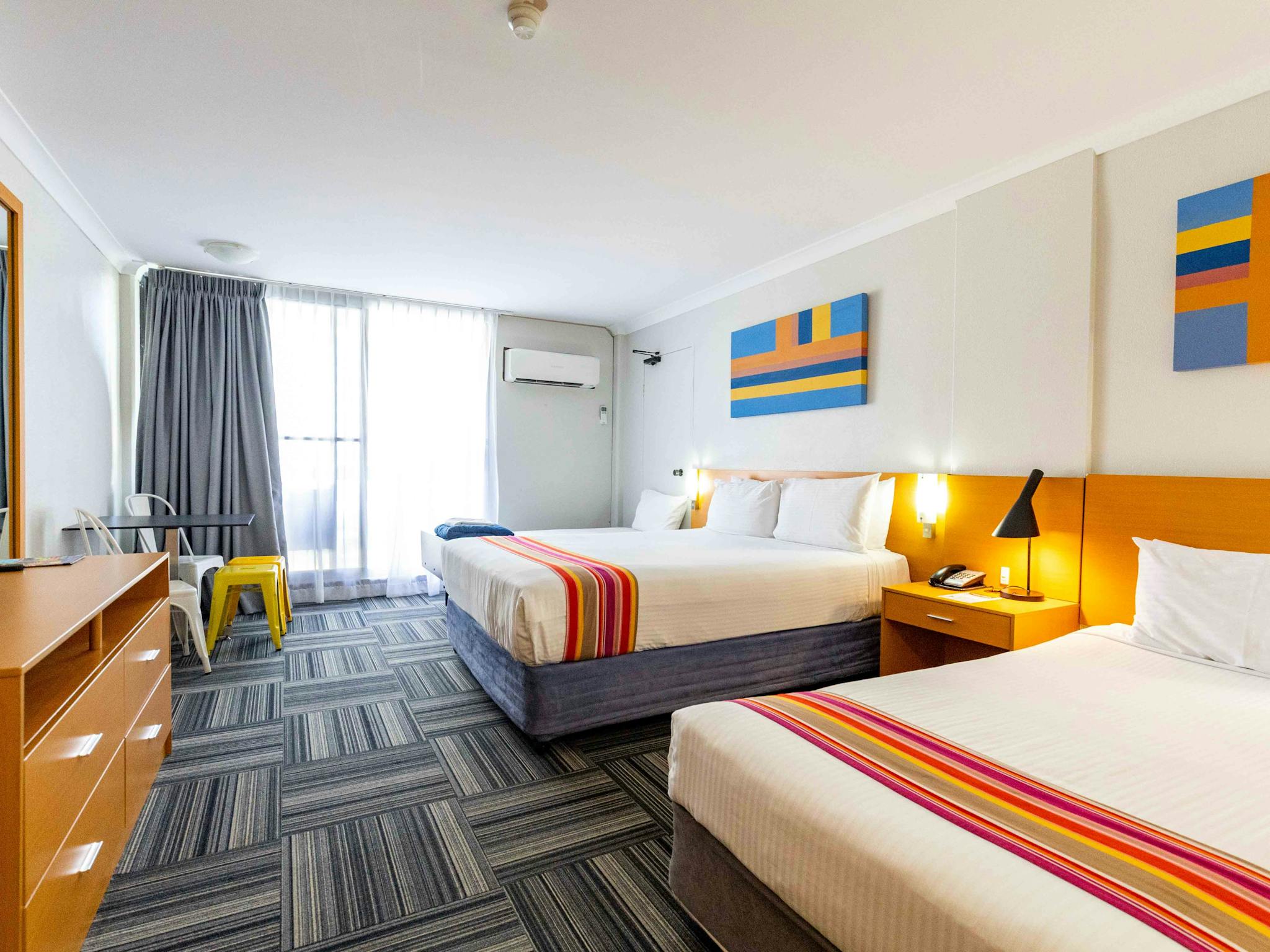 A room with a queen bed and 1 single bed with cabinets and a table and with two chairs A room with a queen bed and 1 single bed with cabinets and a table and with two chairs