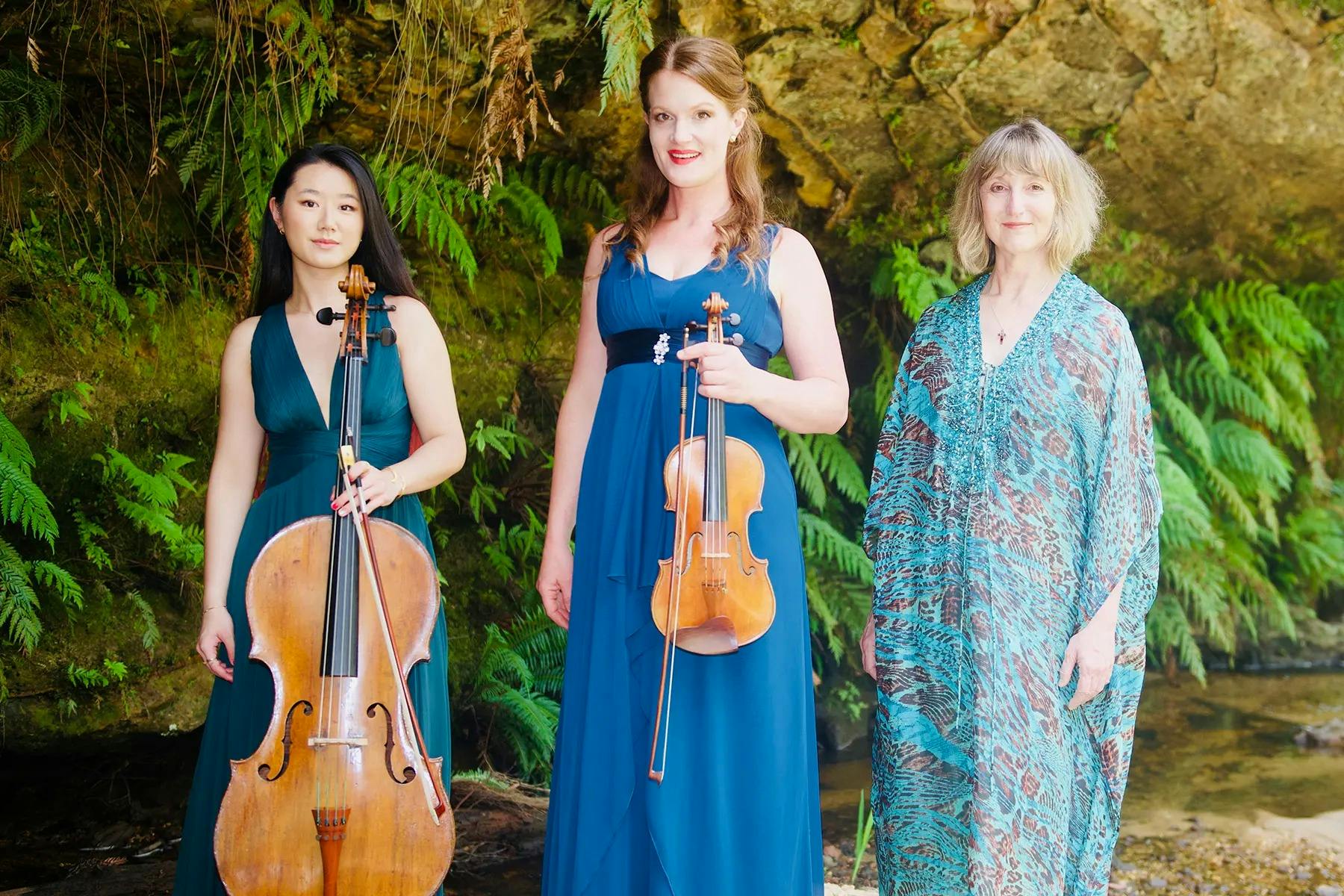 Three artists stand together with a backdrop of lush trees