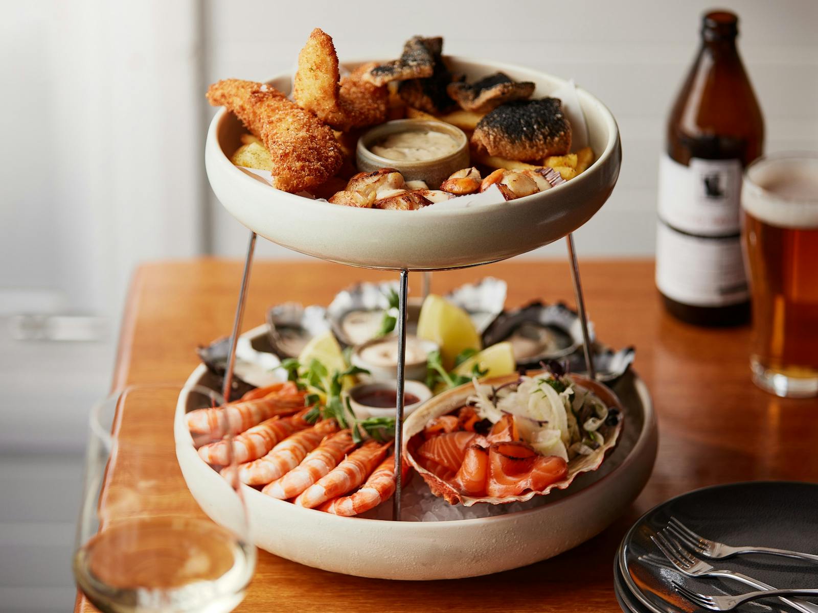 A two-tiered seafood platter featuring oysters, prawns, smoked salmon, scallops, squid, and fish.