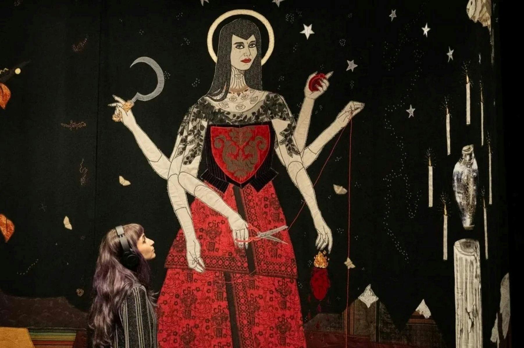 Image of a textile artwork showing a woman standing in a red dress and six arms