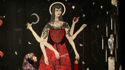 Image of a textile artwork showing a woman standing in a red dress and six arms