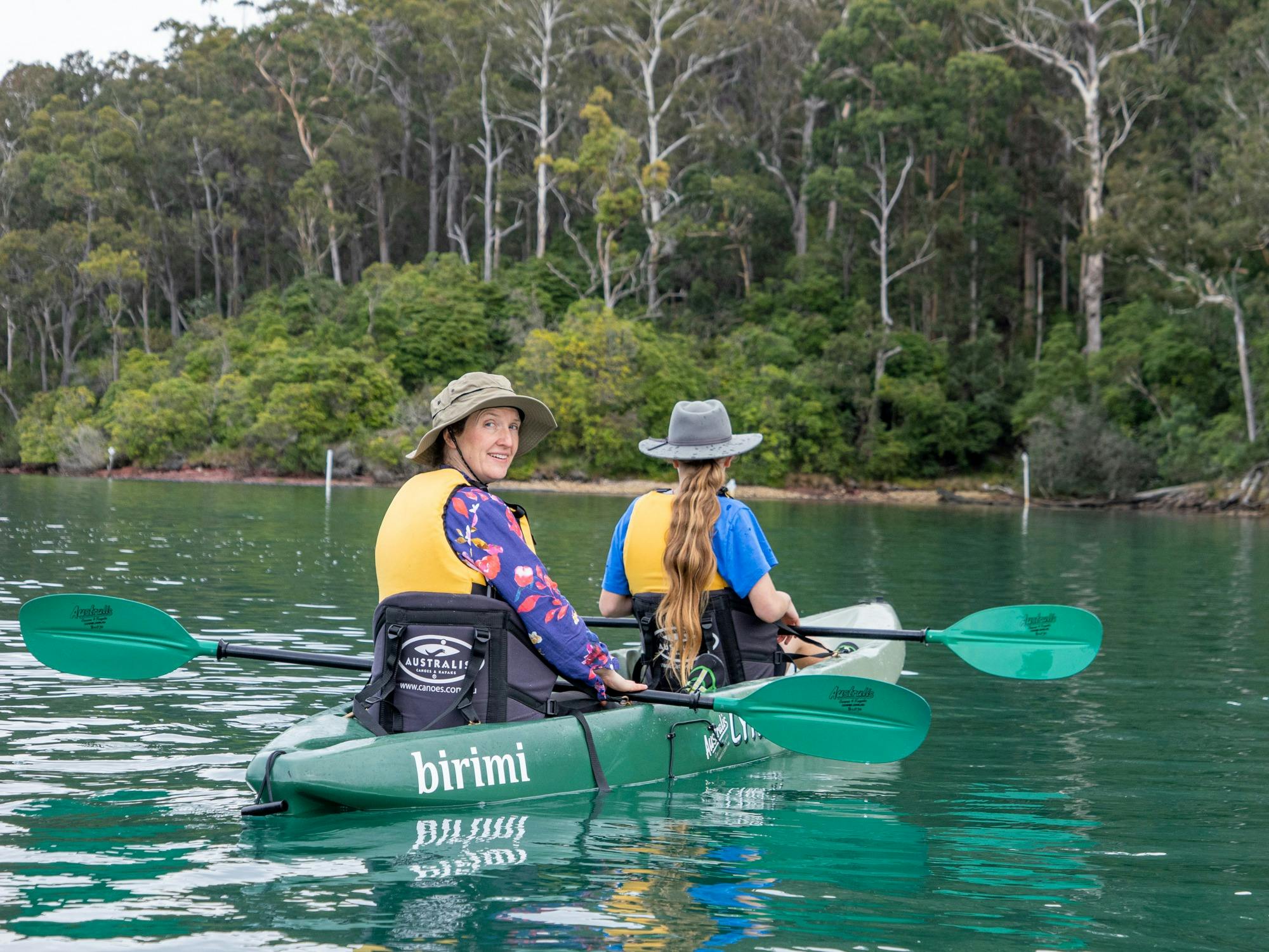 Mother and daughter in a green kayak, smiling and looking back at the camera.