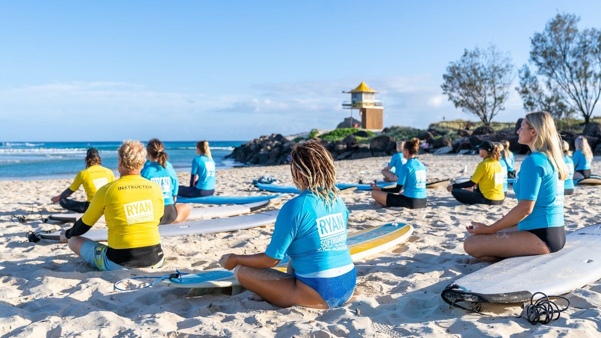 Surf school group meditating on beach.