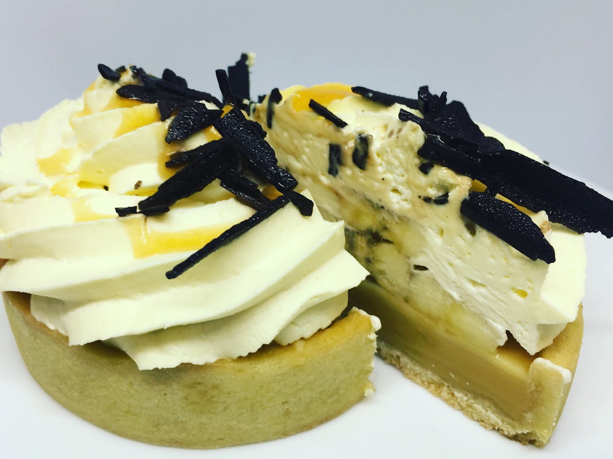 Banoffee pie cut in half and showing layers of caramel, banana, fresh cream, topped with choc flakes