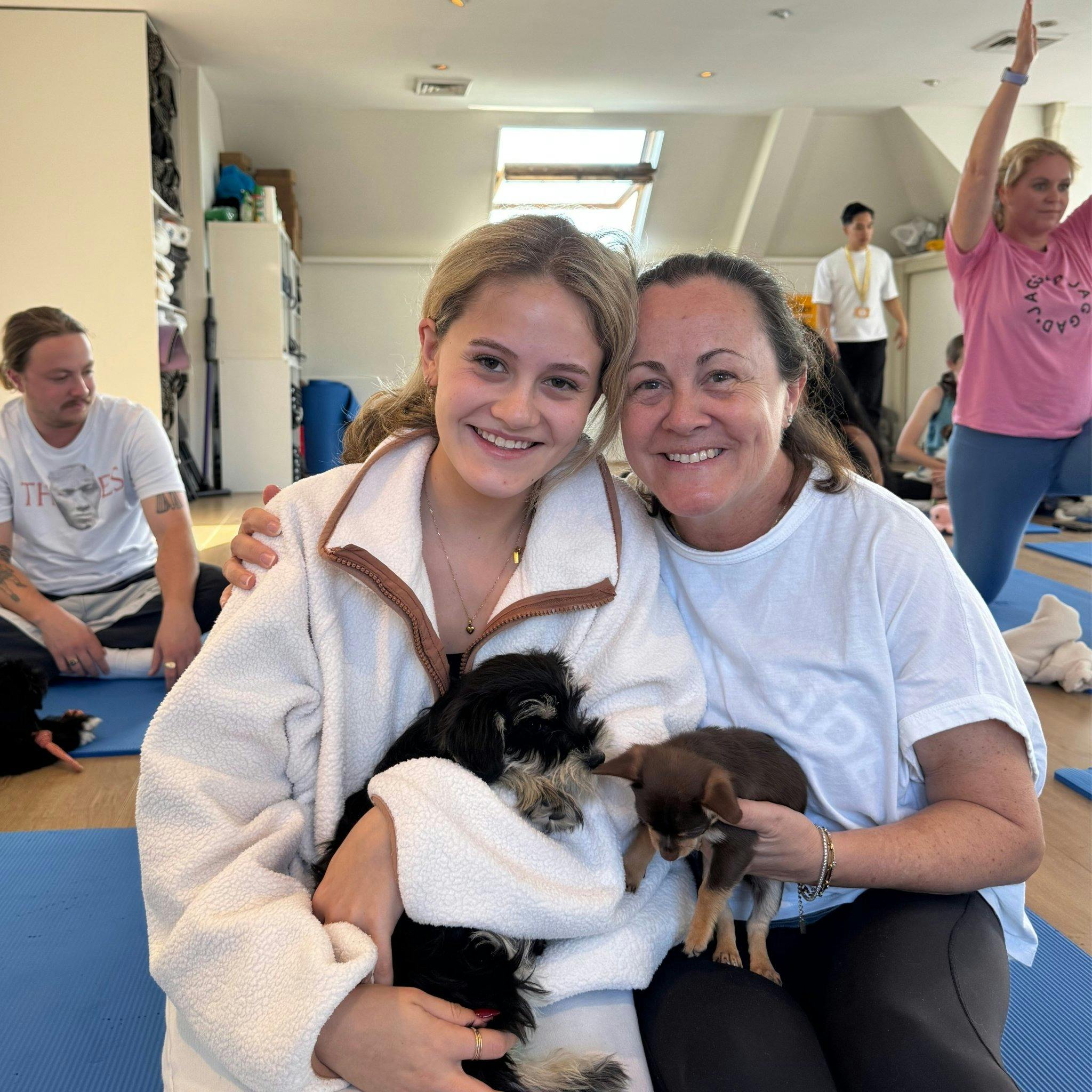 A woman and young girl sitting on blue mats smiling with a small black and white puppy at Doga Sydne
