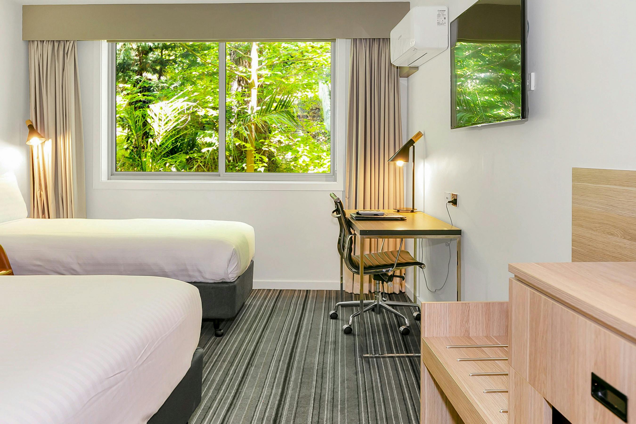 Guest accommodation room, with king bed and single bed, desk and chair, and window with garden view.