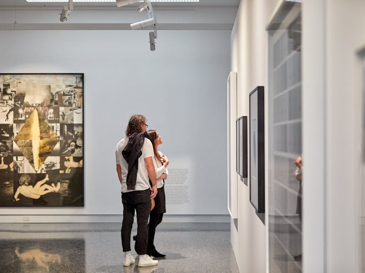 Two visitors view photography in a wide open gallery space