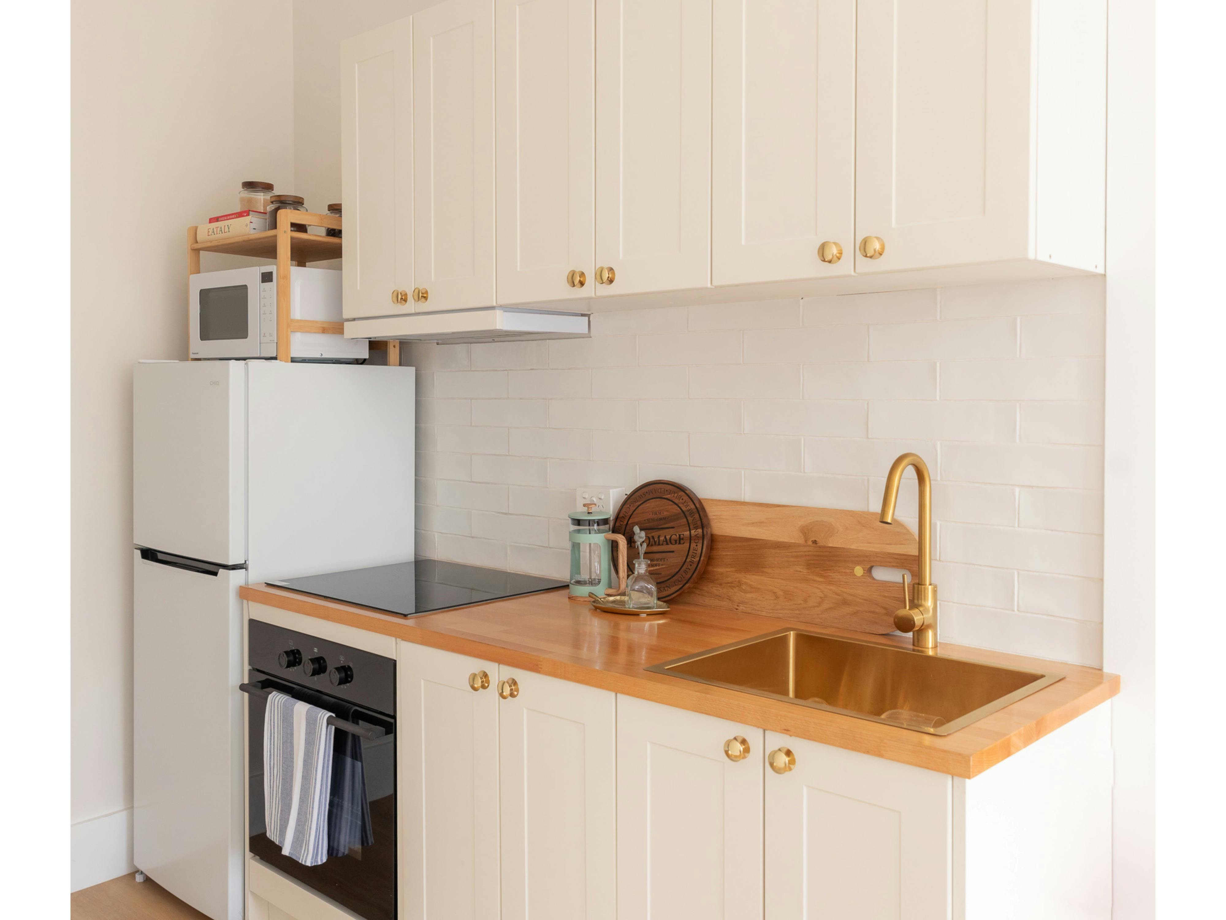 White kitchen, gold sink, tap and knobs, black oven, fridge, microwave, cook top