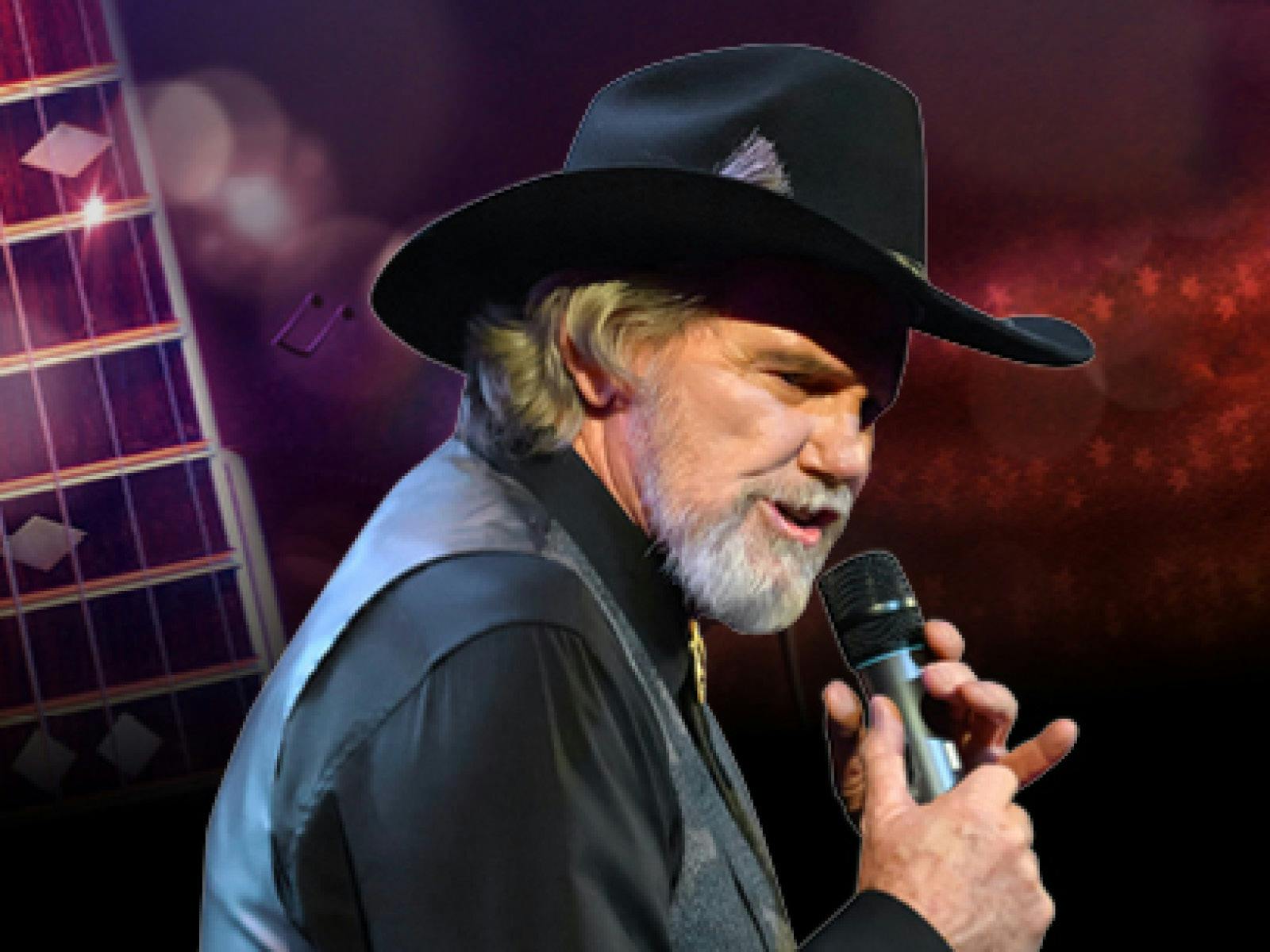 A bearded man wearing a black western hat and vest, singing into a microphone