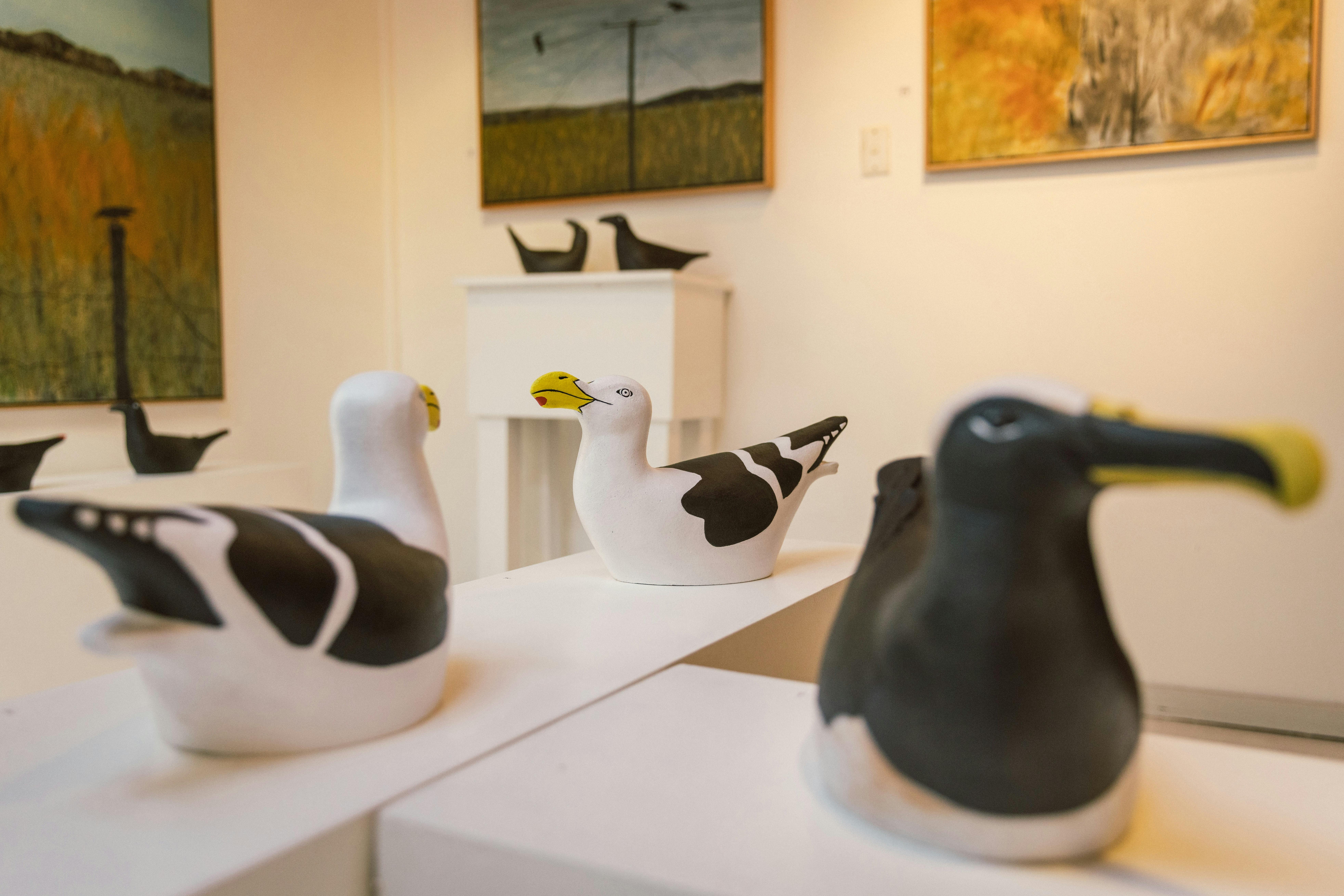 Ceramic seabirds in the foreground sit on plinths with landscape paintings on the wall behind.