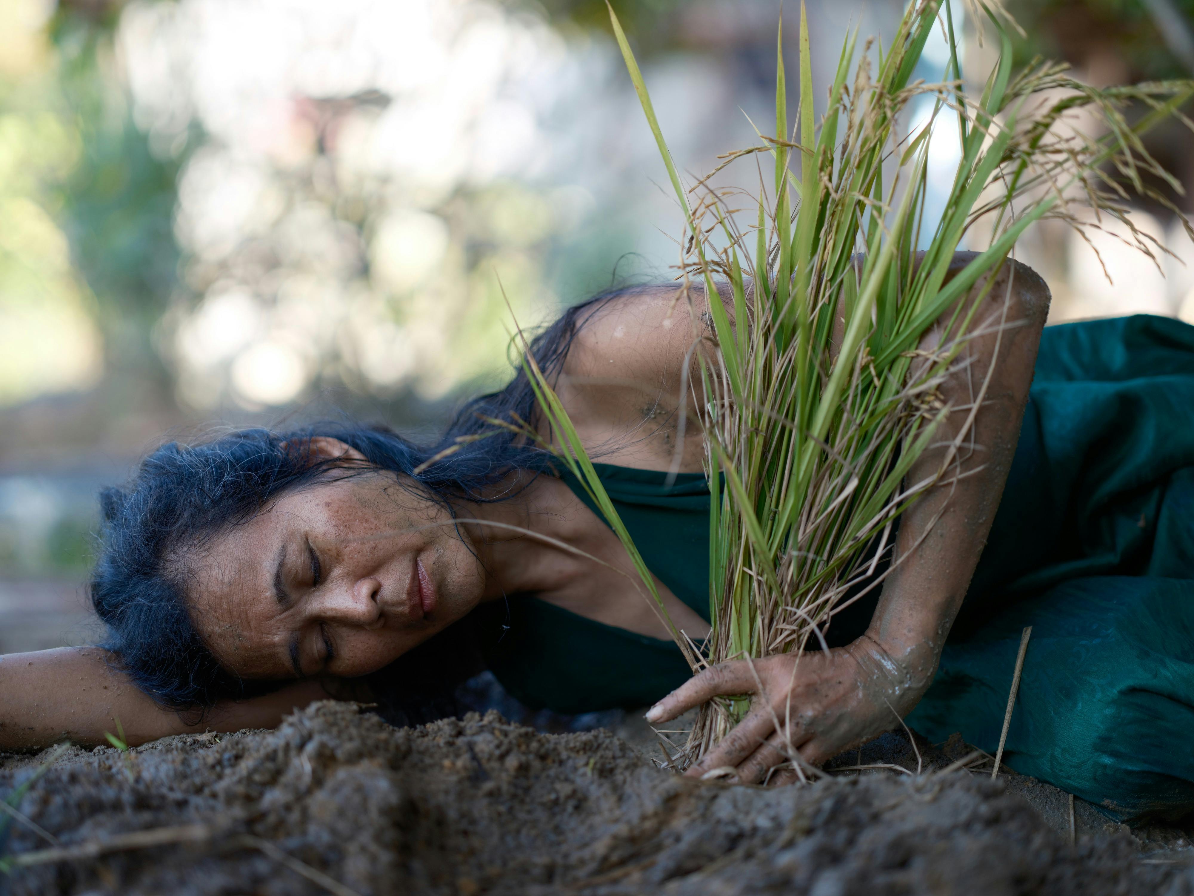 dark haired woman lying on soil holding grass