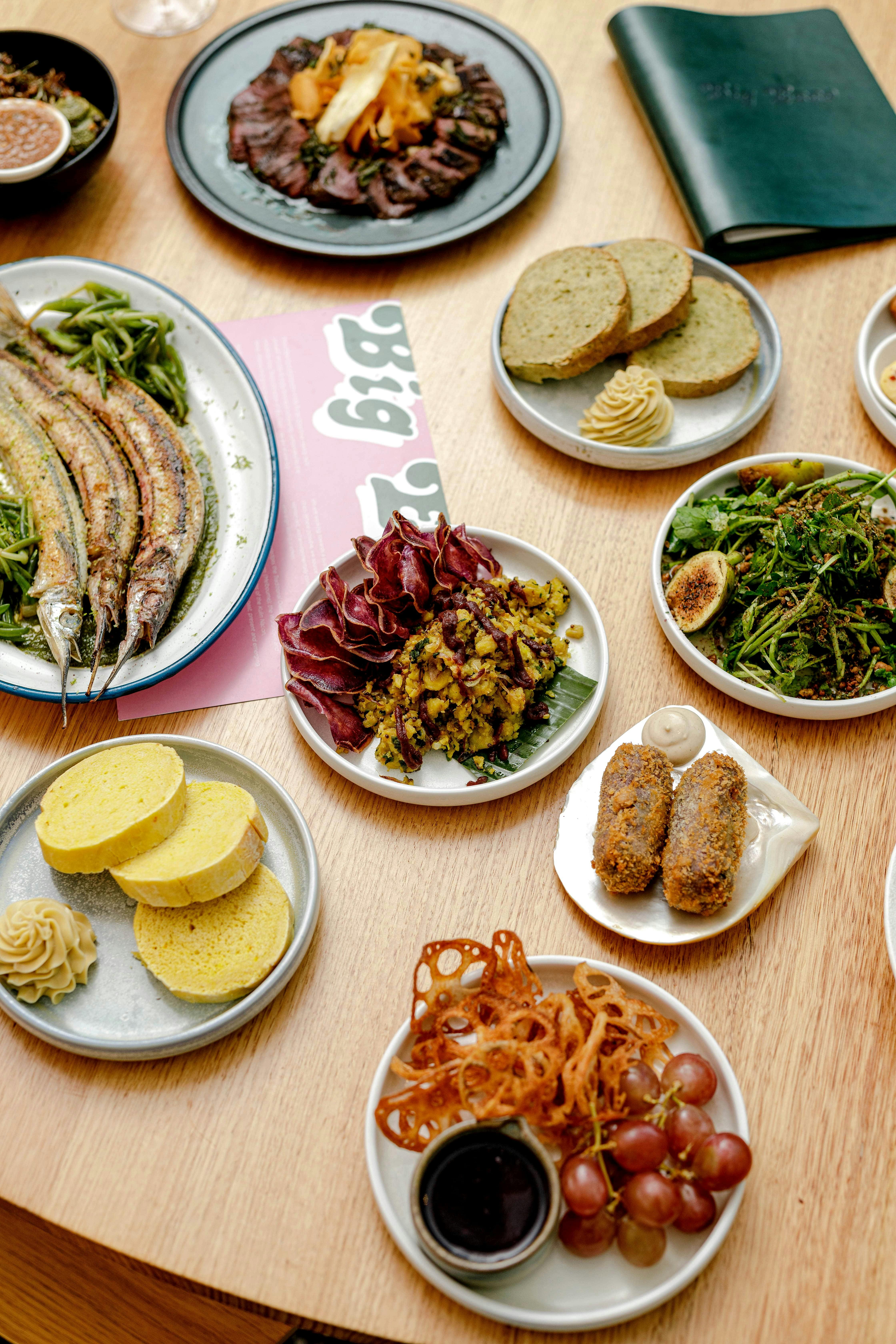 Wooden table with numerous plates of colourful food and pink menu underneath