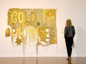 A woman dressed in black views at a large gold tapestry baring the words Golden Promise