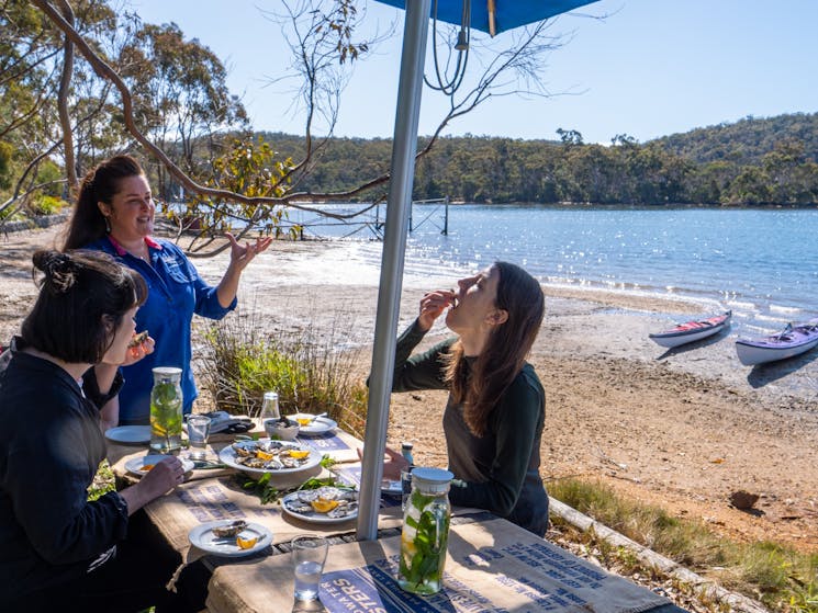 Two guests tasting oysters with kayaks in the background