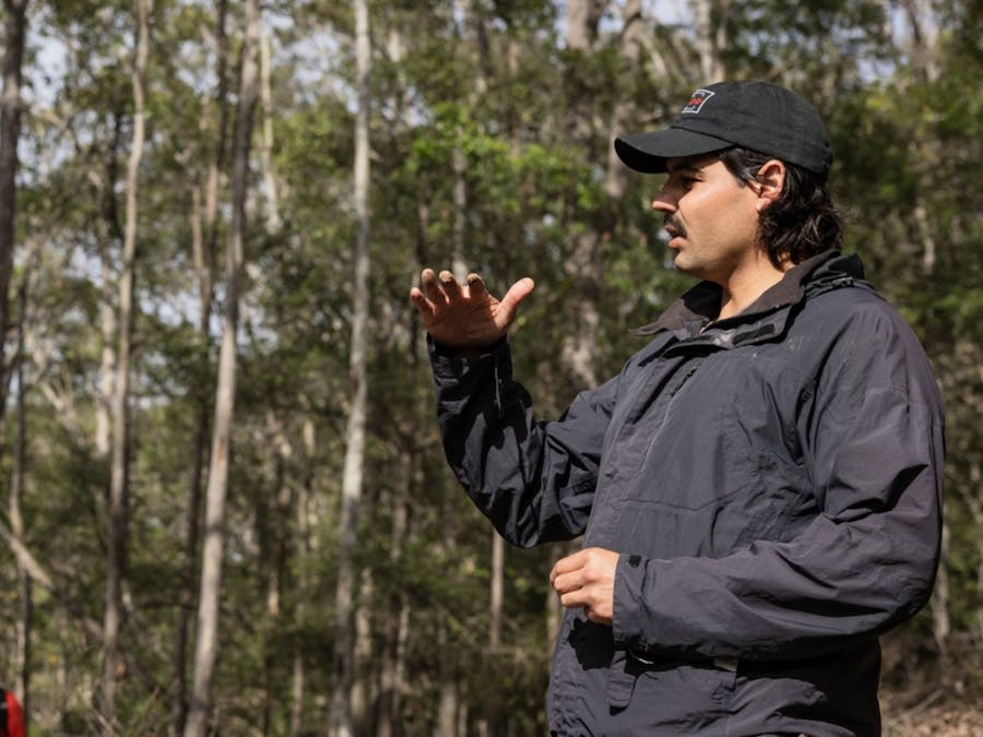 Joel stands in a forest, leading a cultural walk