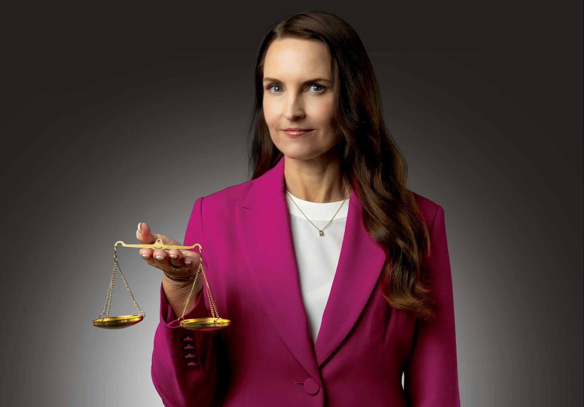 A professional woman in a pink suit holds the scales of justice
