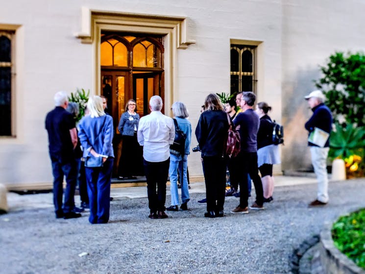 Visitors gather out the front of an historic 1830s mansion. The lights illuminate the front door.