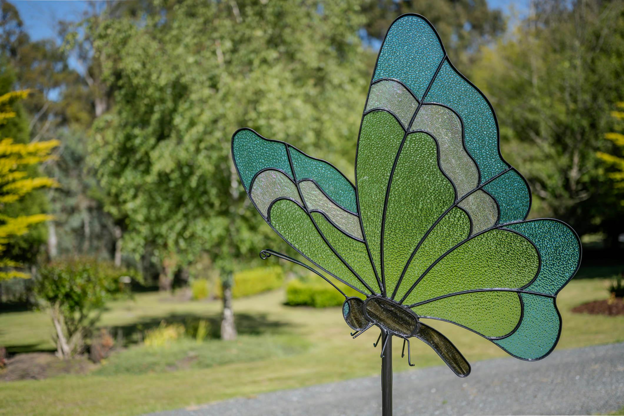 Stained glass butterfly sculpture mounted on a steel stem outdoors.