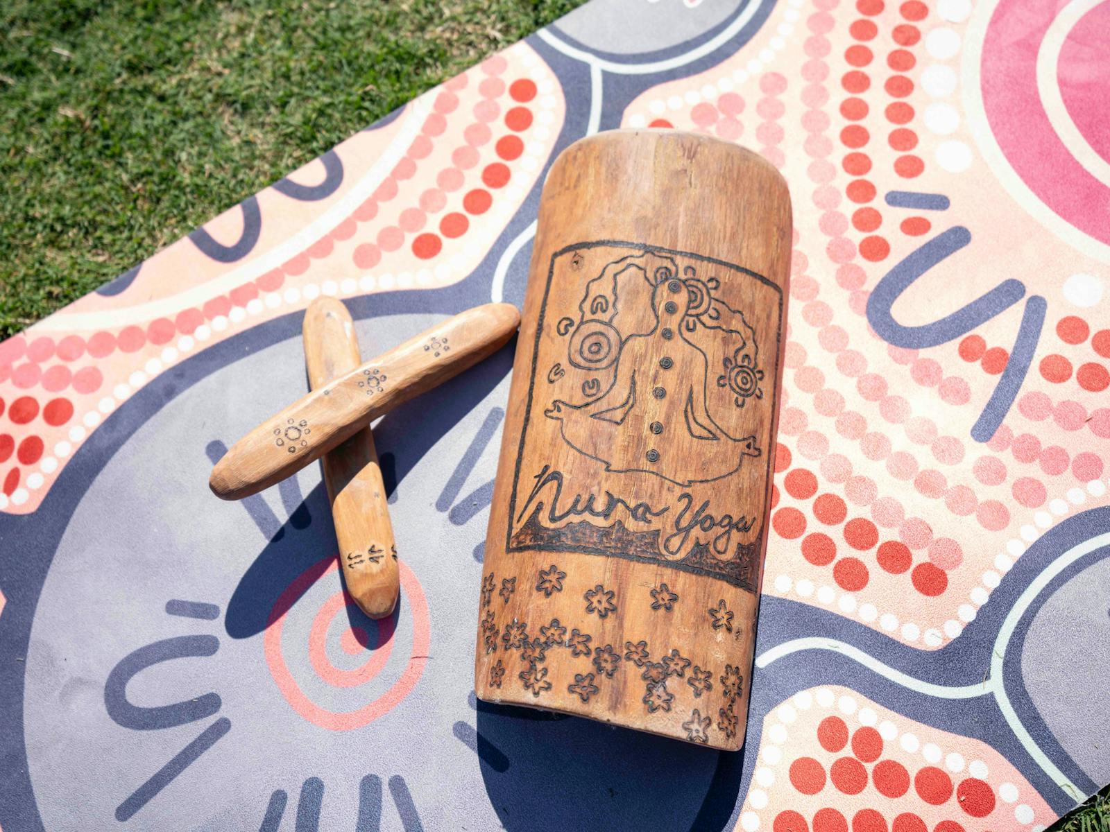 A Indigenous designed yoga mat with a coolamon & clapping sticks