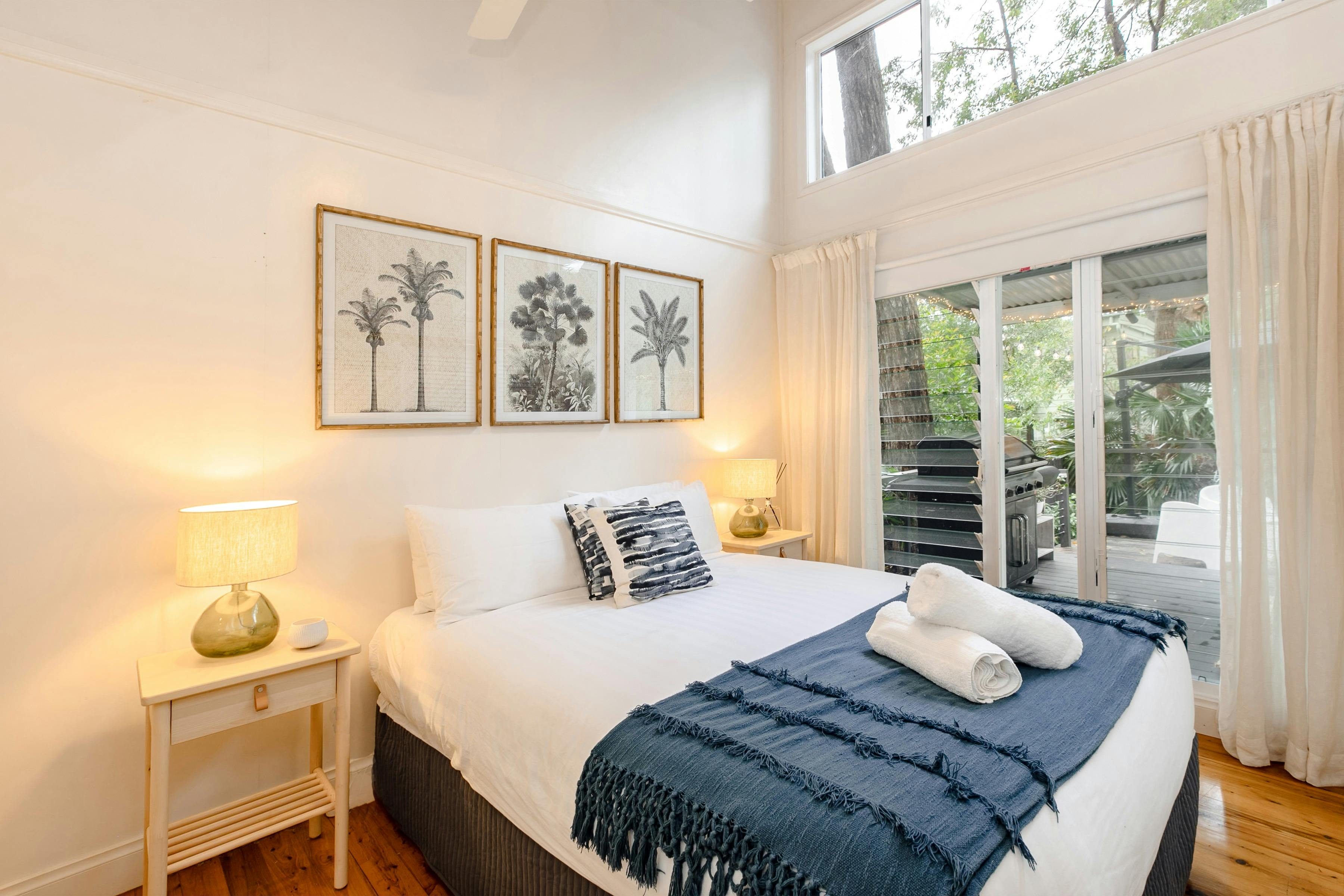 Bedroom with bedside table, white fresh linen and window looking out to deck