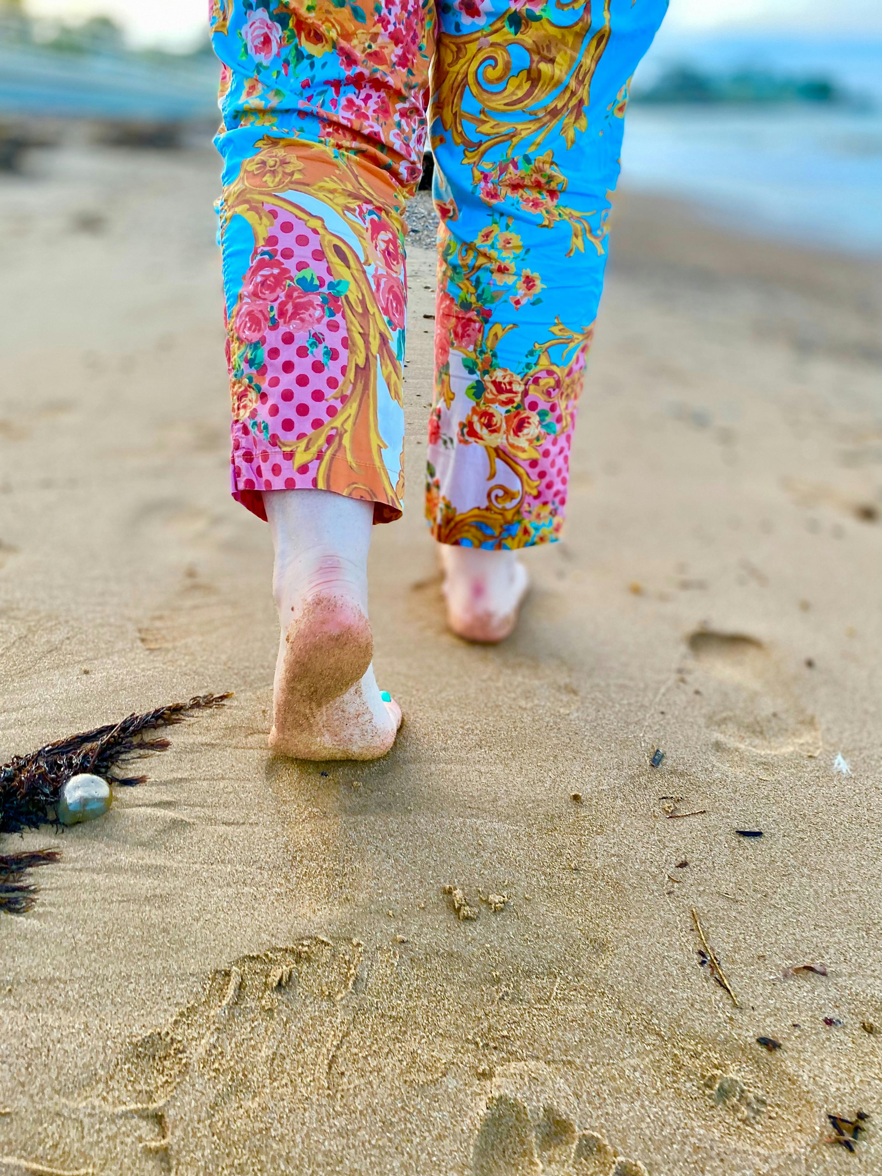 Bare feet imprinting the sand on Penguin Beach, by woman wearing colourful trousers.