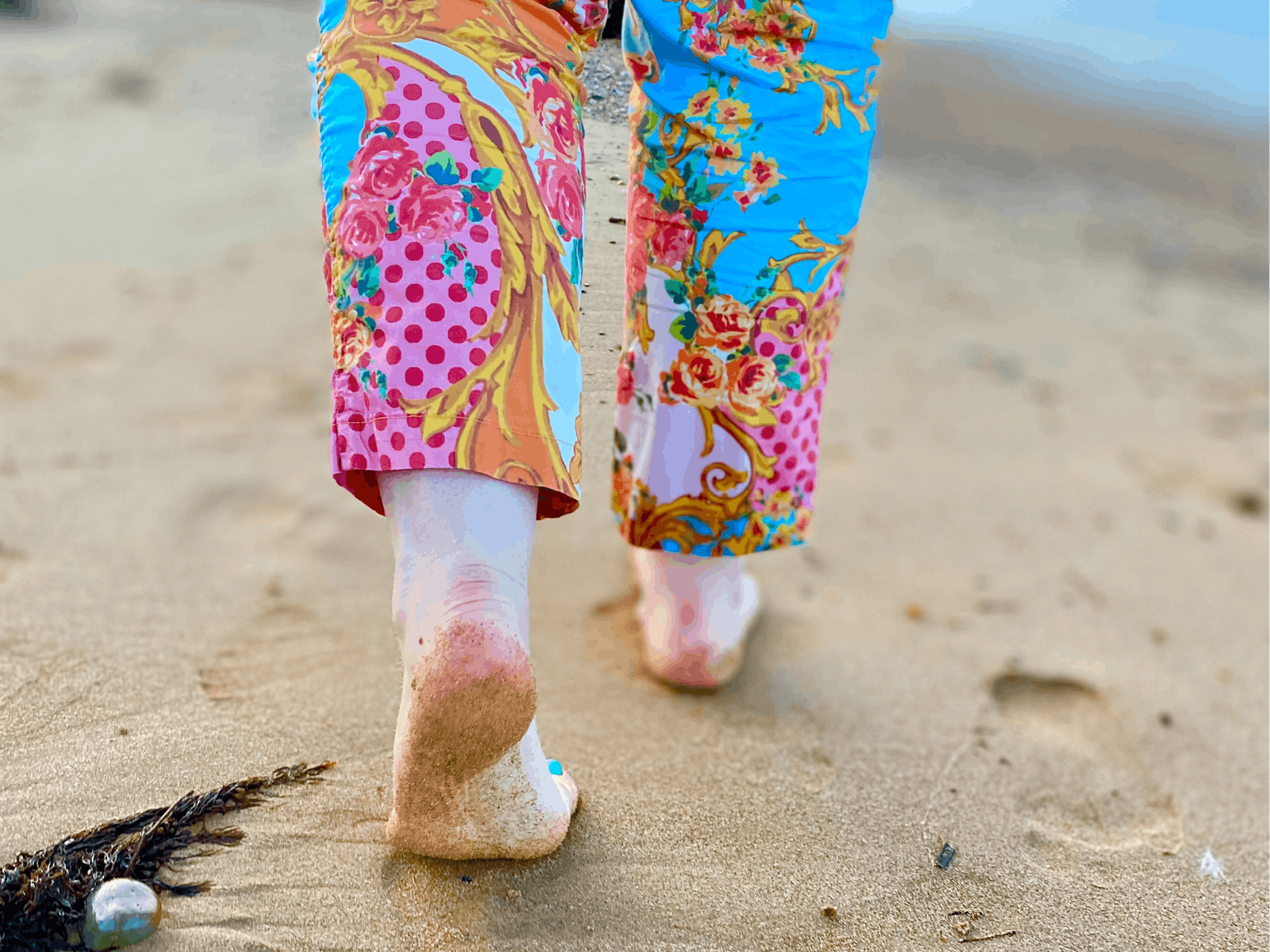 Bare feet imprinting the sand on Penguin Beach, by woman wearing colourful trousers.