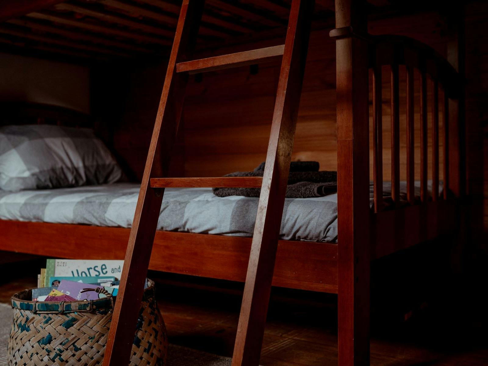 Timber bunk bed with checked bedding, ladder, and basket of children’s books nearby