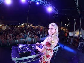 DJ Emma Peters smiling at the camera while she DJs on the main stage with crowd in the background