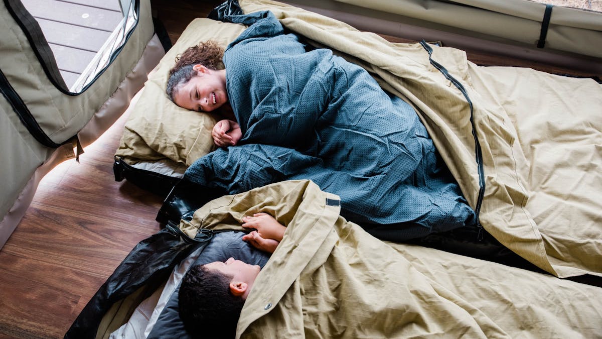 Smiling children tucked into swags inside of glamping tent