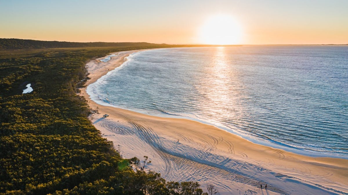 Sunset over Main Beach, North Stradbroke Island (Minjerribah), with tyre tracks across golden sand.