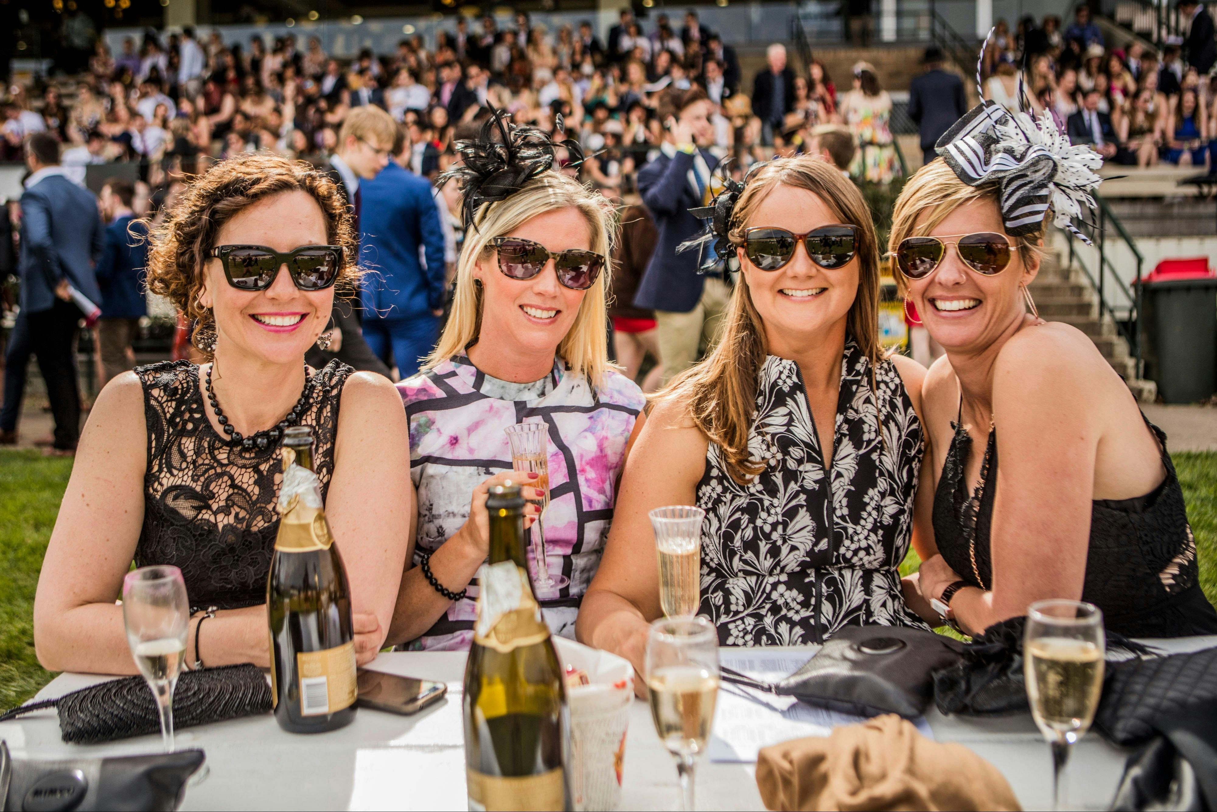 Four ladies dressed for the races enjoying champagne