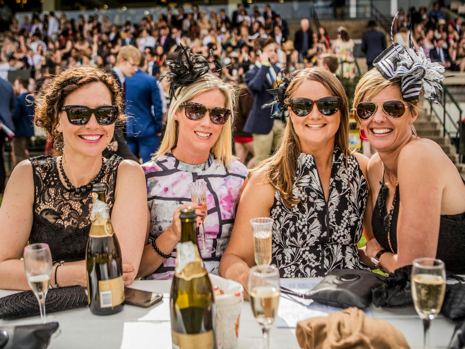 Four ladies dressed for the races enjoying champagne