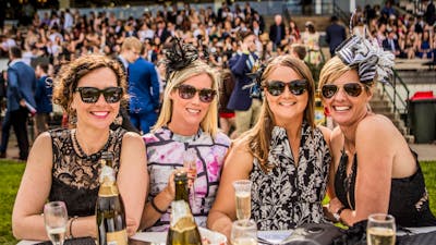 Four ladies dressed for the races enjoying champagne