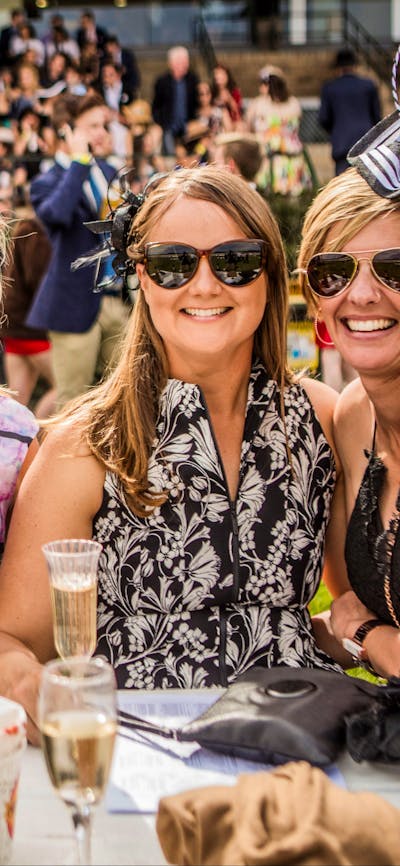 Four ladies dressed for the races enjoying champagne