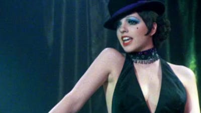 Woman with short black hair, hat and black top in the middle of singing looking over right shoulder