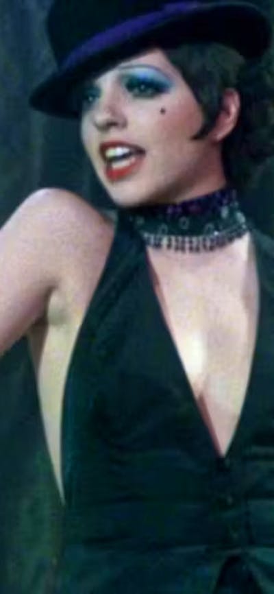 Woman with short black hair, hat and black top in the middle of singing looking over right shoulder