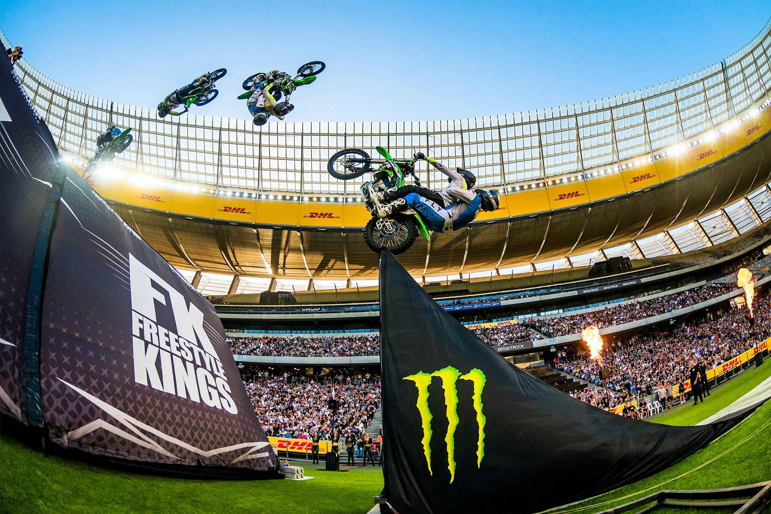 A motorcycle rider does a backflip over a jump in an arena